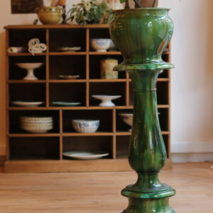 Beau meuble de rangement à casiers en pin massif, datant du début du XXᵉ siècle. Composé de 18 compartiments (12 petits et 6 grands), il offre une capacité de rangement généreuse et décorative, idéale pour une vaisselle ancienne, des livres ou des objets de collection. Finition cirée, plateau supérieur à bords arrondis et base soulignée d’une élégante plinthe moulurée. Dimensions : hauteur 100 cm – longueur 115 cm – profondeur 32 cm. En bon état général, avec quelques traces anciennes d’usage dans deux casiers (taches d’huile ou de gras). Colonne jardinière Art Nouveau en faïence émaillée flammée vert, Sarreguemines, vers 1900